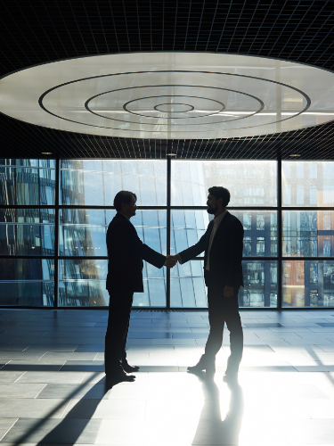 Two men shaking hands in a lobby in front of big windows